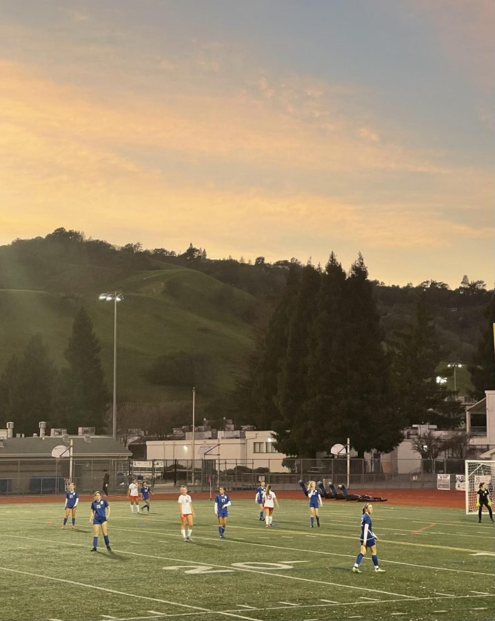 Junior Varsity players roam the field at sunset. 