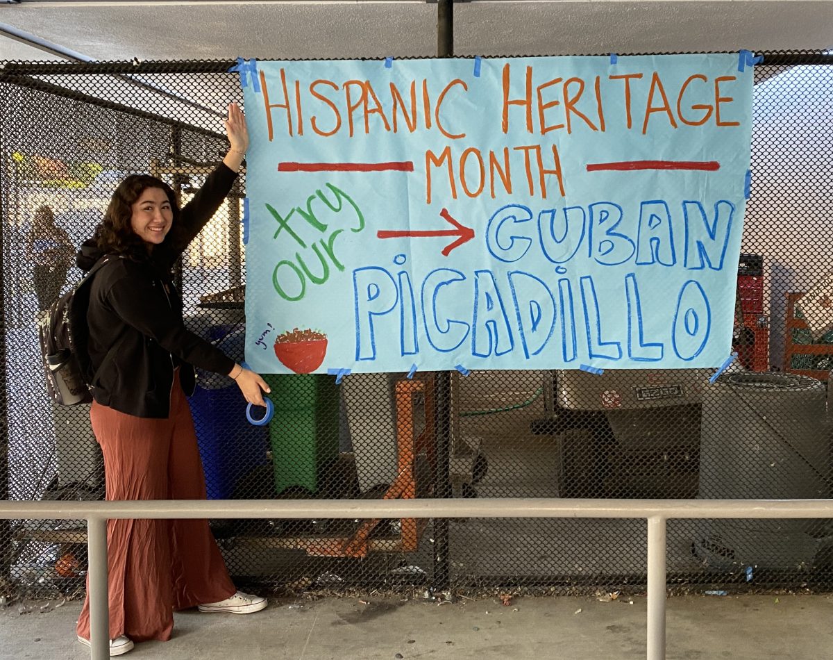 Latinos Unidos club member standing in front of Cuban picadillo sign.